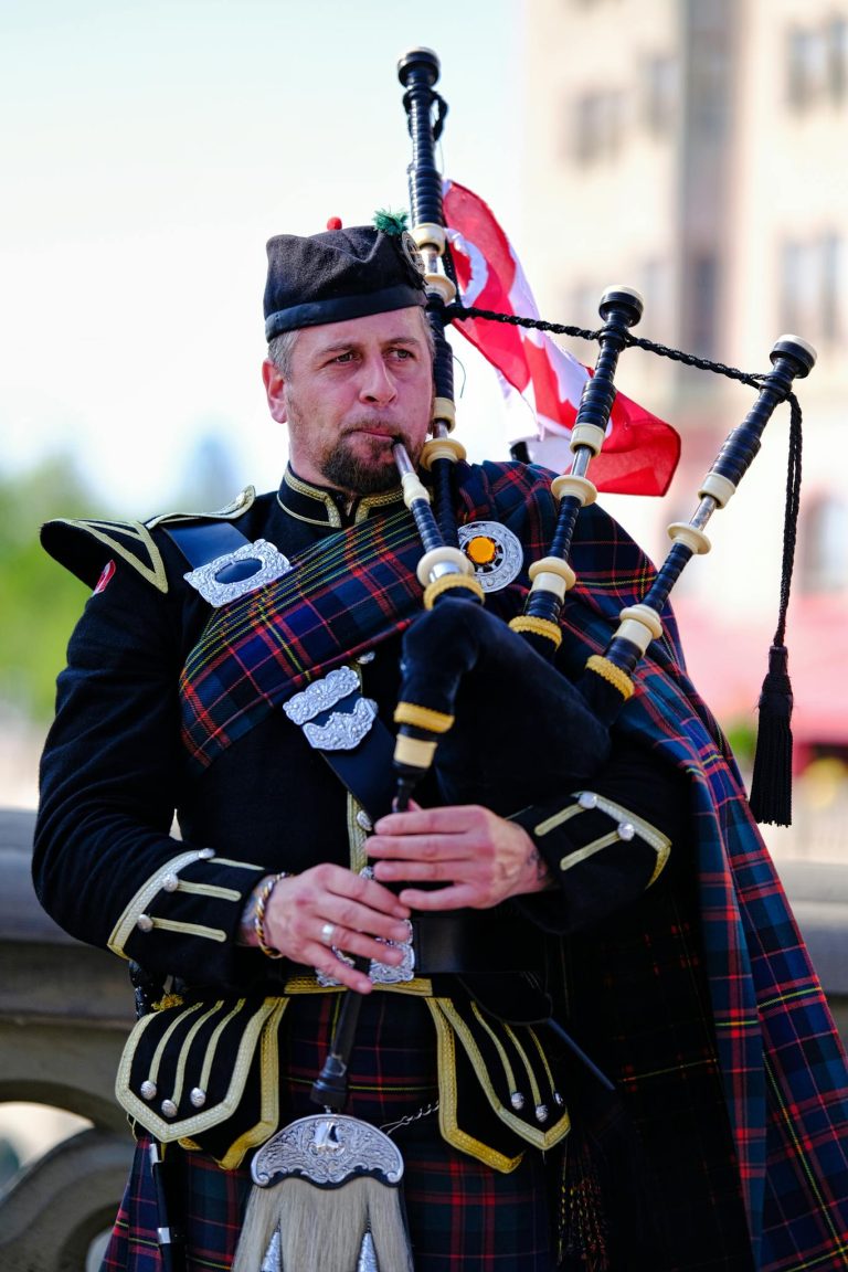 A Scottish bagpiper dressed in traditional attire playing outdoors in a cultural celebration.