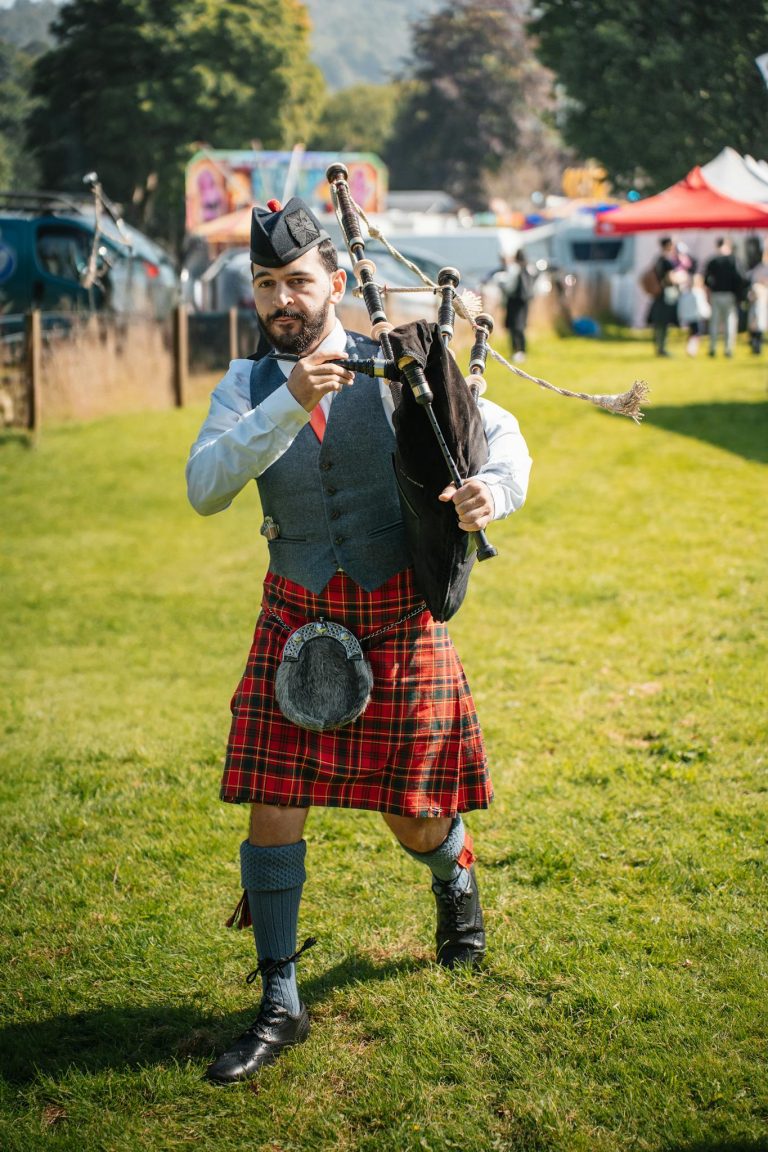 A Scottish bagpiper in traditional attire performs outdoors at a cultural festival.