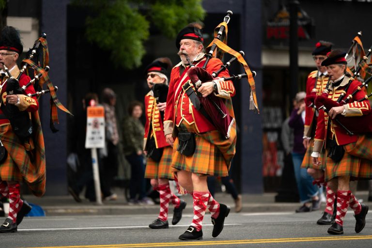 Men in traditional Scottish attire play bagpipes in a lively parade.