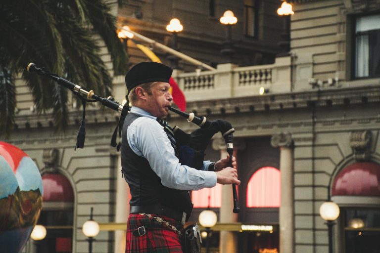 Street musician playing bagpipes in a cityscape setting during the day.